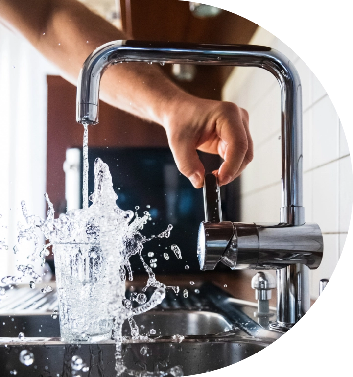 Eine Hand bedient einen Wasserhahn, um ein Glas mit Wasser zu füllen